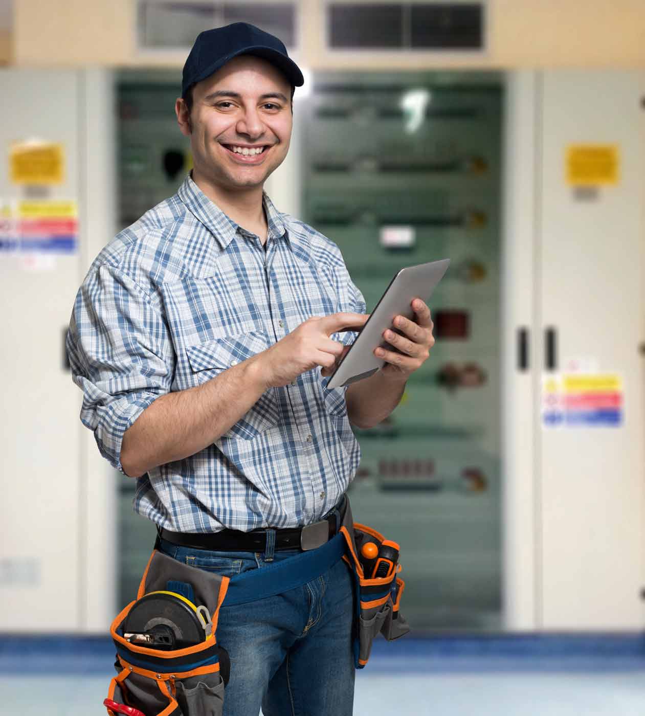 Freundlicher Hausmeister oder Elektriker mit Tablet steht vor einem Schaltschrank – Handwerkerjob an Schulen in Dresden