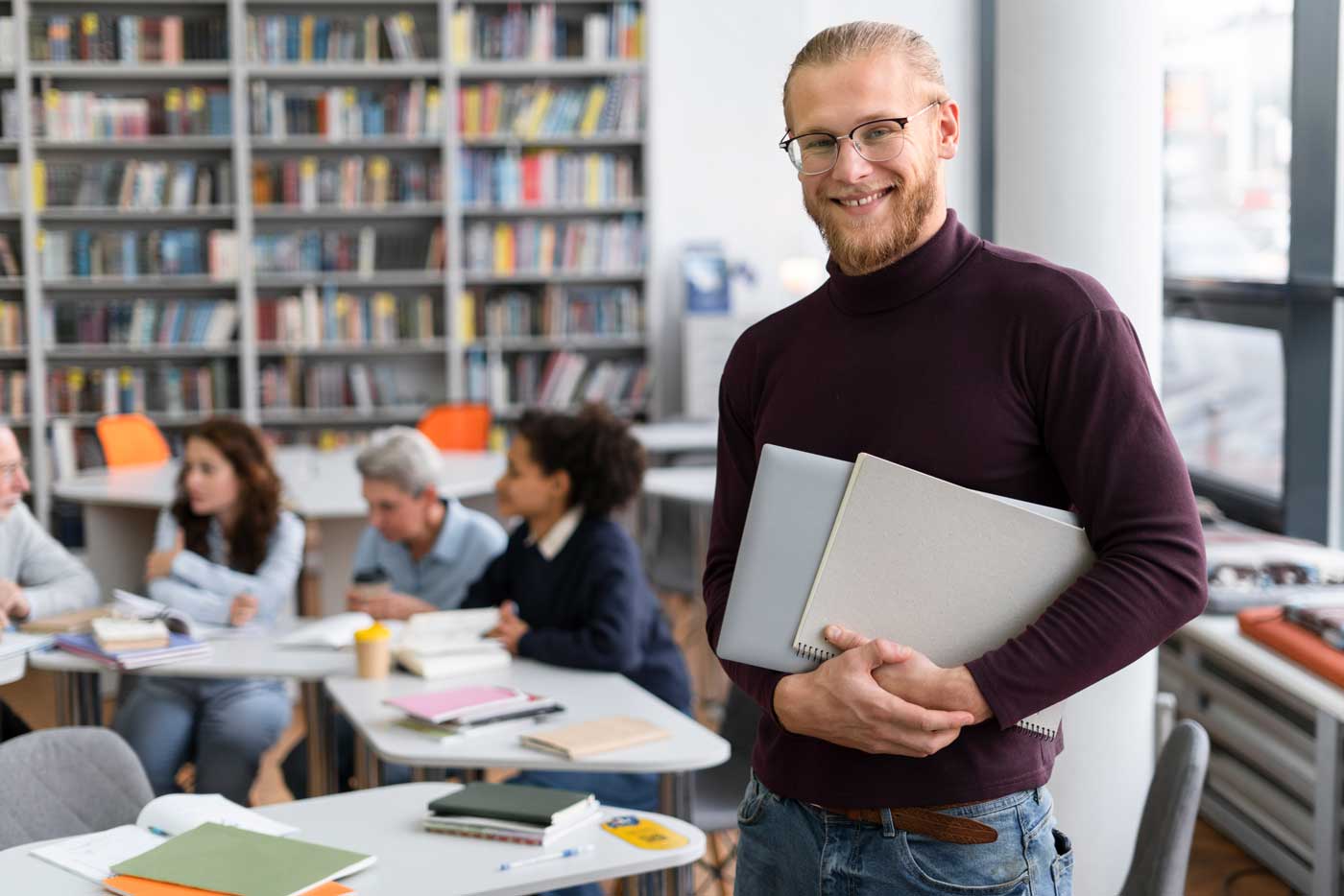 Erfahrener Dozent steht mit Ordnern in der Bibliothek eines Klassenzimmers und lächelt – Karriere und Jobs in Dresden