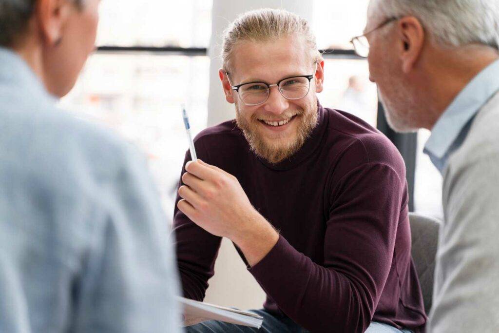 Männlicher Lehrer oder Dozent lächelt in einer Besprechung und tauscht sich mit Kolleginnen aus – Bildung und Jobs in Dresden