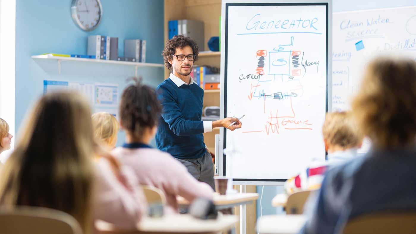 Physiklehrer erklärt einer Schulklasse anschaulich einen Generator an der Tafel