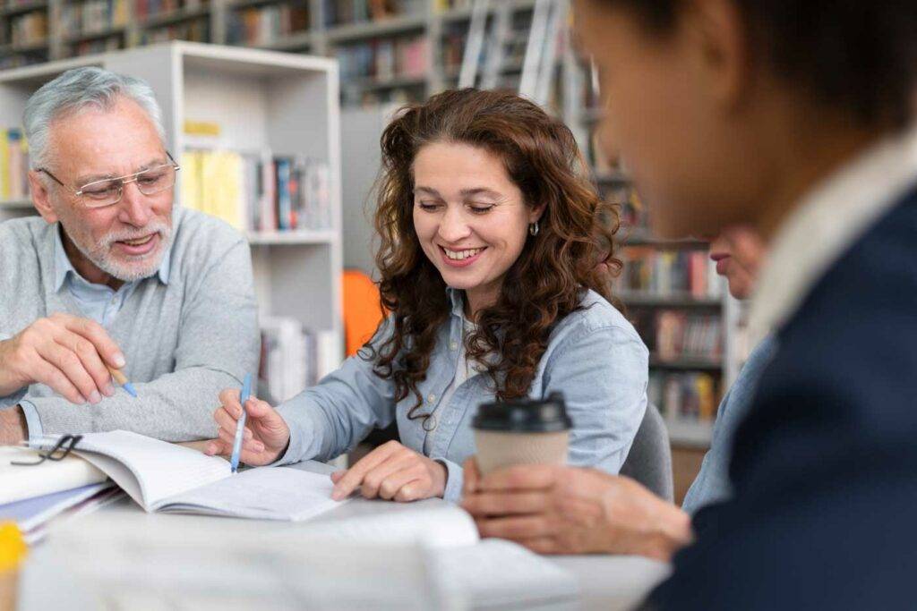 Erfahrener Lehrer unterstützt Kollegin beim Planen des Unterrichts in der Bibliothek der HOGA Schule Dresden