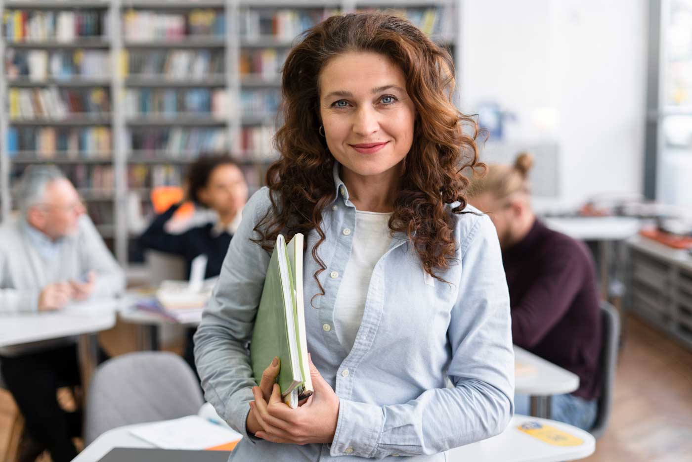 Lehrerin mit lockigem Haar hält Lehrbücher im Klassenzimmer – Stellenangebote für Pädagogen in Dresden