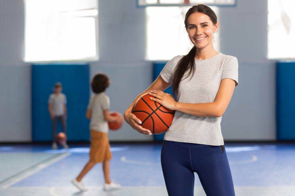 Sportlehrerin mit Basketball verschränkt die Arme in der Turnhalle der HOGA Schule Dresden